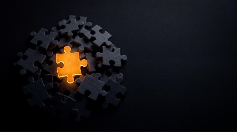 One glowing amber puzzle piece completing a circle of dim grey pieces on a dark background — the missing piece AI is still looking for